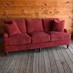 a red couch sitting on top of a wooden floor next to a wood paneled wall