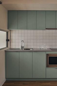 an empty kitchen with green cabinets and white tile backsplash, wood flooring