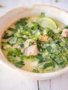 a white bowl filled with soup and garnished with cilantro, parsley and lime