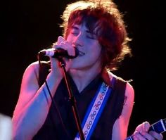 a young man holding a guitar and singing into a microphone while standing in front of a microphone