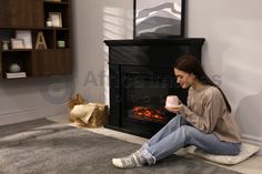 Beautiful young woman with cup of hot drink sitting on floor near fireplace at home. Space for text Sitting On Floor, Relaxation Room, Home Space, Happy Mothers, Hot Drink