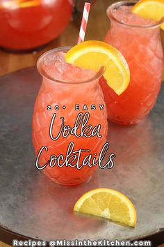 two glasses filled with vodka cocktails sitting on top of a metal tray next to lemon wedges