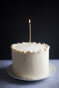 a white frosted cake with a single candle sticking out of it's center