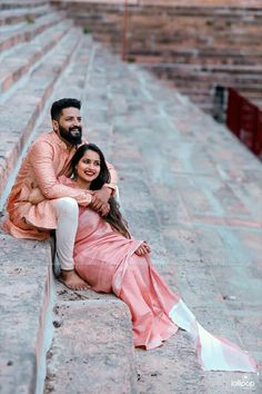 a man and woman sitting on the ground in front of some steps with their arms around each other