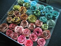 there are many different colors of rolled flowers in the glass box on the table top