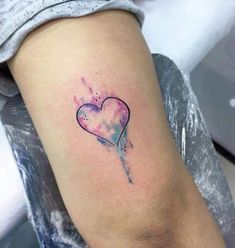 a heart shaped tattoo on the leg with watercolor paint splattered over it