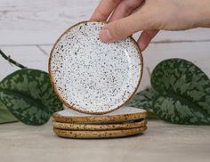 a hand is holding a white plate on top of three wooden coasters