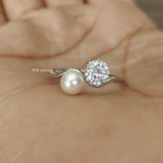 a close up of a person's hand holding a ring with a pearl on it