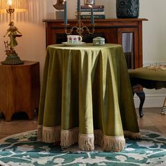 a green table cloth with tassels sits on a round rug in front of a wooden cabinet