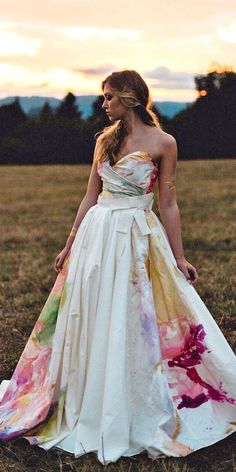 a woman standing in a field wearing a white dress with colorful flowers on the skirt