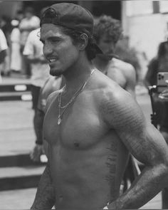 a man with no shirt on standing in front of a parking meter and wearing a hat