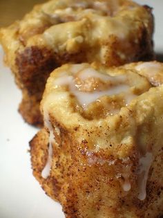 three cinnamon rolls on a white plate with icing drizzled over them