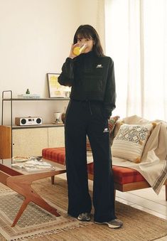 a woman standing in a living room while eating an orange slice with her hand on her mouth