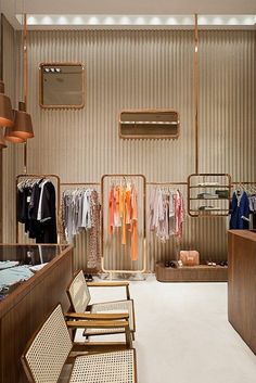 the inside of a clothing store with clothes hanging on racks and chairs in front of it