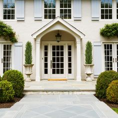 a large white house with blue shutters and trimmed bushes on the front door area