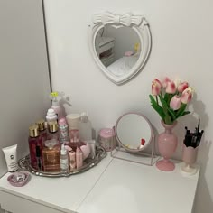 a white dresser topped with lots of beauty products and pink vase filled with tulips