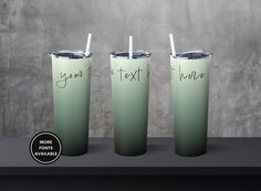 three green tumblers with straws in them sitting on a table next to a gray wall