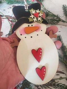 a hand holding a snowman ornament with hearts