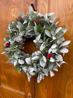 a wreath with red berries and greenery hangs on a wooden door