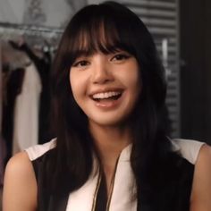 a woman with long hair smiling and wearing a white top in front of a rack of clothes