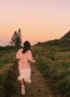 a woman running down a dirt path in the grass at sunset or dawn with her hair blowing back