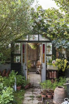 a small garden shed with potted plants in the front and an open door to it