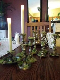 a dining room table with candles and moss on the top, in front of a mirror