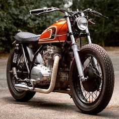 an orange and black motorcycle parked on top of a gravel road next to some trees