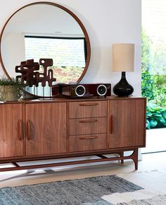 a large round mirror sitting on top of a wooden sideboard next to a lamp