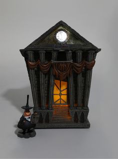 a figurine with a clock on the top of it's face next to a building