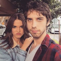 a man and woman standing next to each other in front of a building with cars