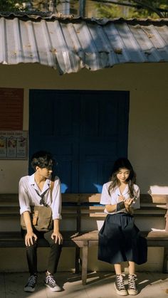 a man and woman sitting on benches in front of a building next to each other