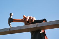 a man holding a hammer over a piece of wood with his right hand on top of it