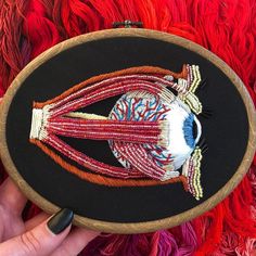 a person holding a black and red embroidered object in front of a colorful wall hanging