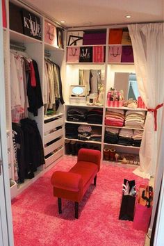 an open closet with pink carpet and clothes on the shelves, including a red chair