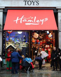 people standing in front of a toy store with christmas decorations on the windows and red awnings