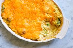 a casserole dish with broccoli and cheese in it on a marble surface