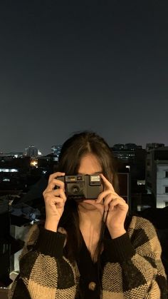 a woman holding up a camera to take a photo in front of the city at night