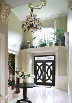 an entry way with a chandelier and flowers in the vase on the table