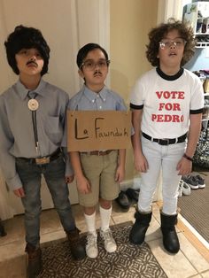 three young boys standing in front of a door holding a cardboard sign