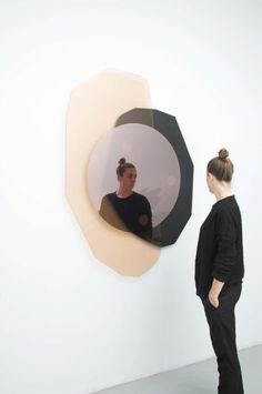 a woman standing in front of a mirror with her reflection on the wall behind it