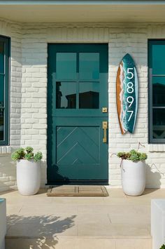 a surfboard sitting on the side of a building next to two planters with succulents