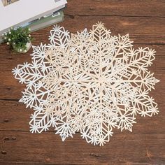 paper snowflakes on a wooden table next to a book and plant in a vase