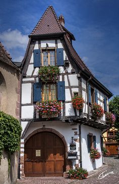 an old house with flower boxes on the roof and flowers growing out of the windows