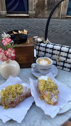 two pastries sitting on top of white plates next to a cup of coffee