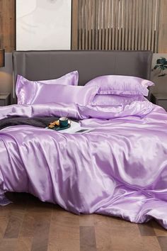 a bed with purple sheets and pillows on top of it in a room that has wooden floors