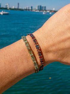 a person's arm with two bracelets on it and the ocean in the background