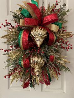 a christmas wreath on the front door with red, green and gold ribbons around it