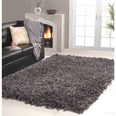 a living room with a black leather couch and gray rug on the floor, fireplace in the background