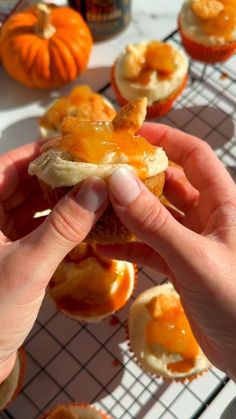 a person is holding up a pastry with orange icing on it and some pumpkins in the background